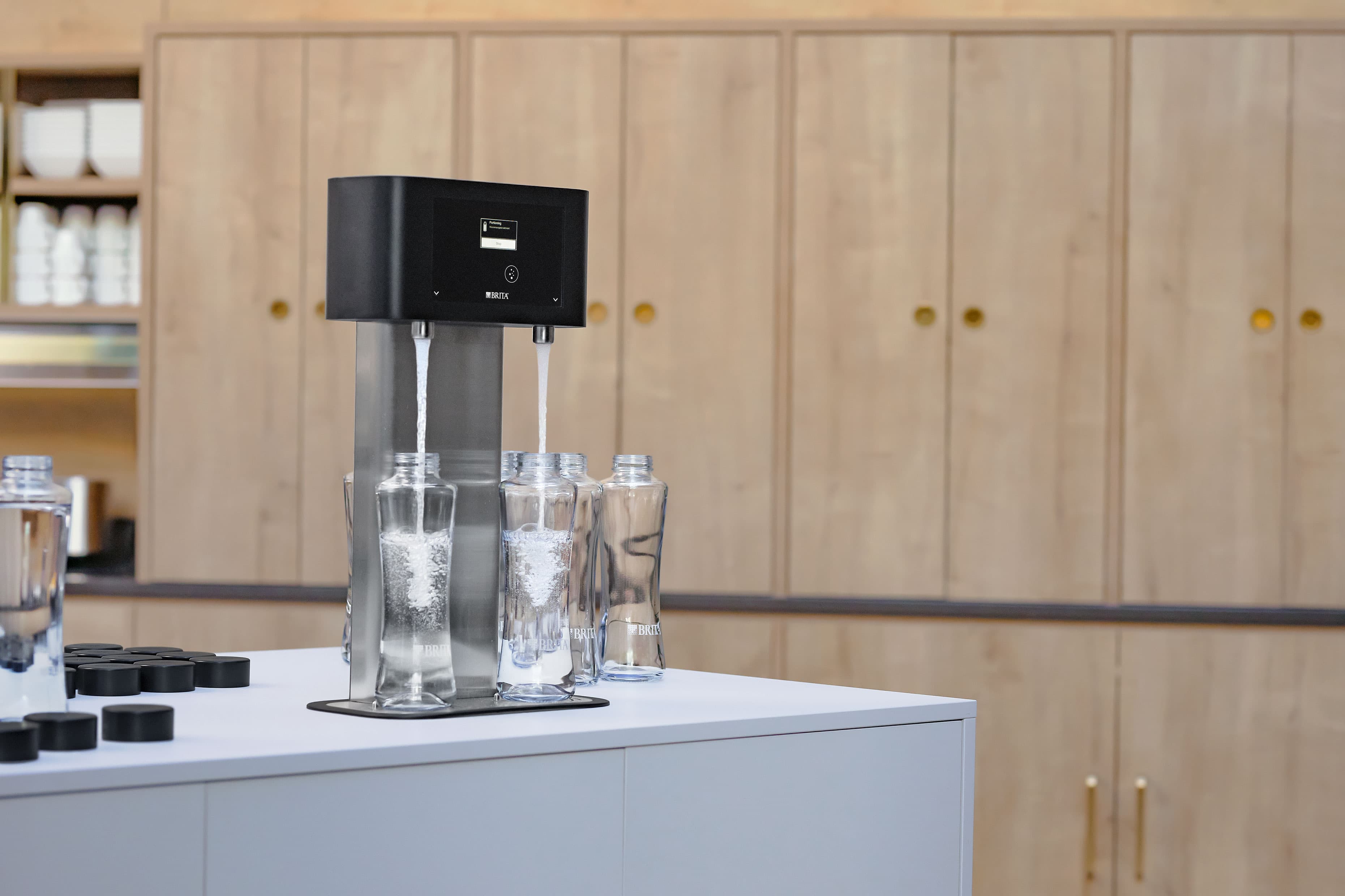 Wasserspender mit zwei Auslässen: Der BRITA Spender füllt zwei Trinkflaschen gleichzeitig, daneben stehen weitere Flaschen mit abgenommenen Deckeln bereit.